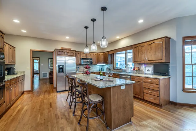 a kitchen with stainless steel appliances granite countertop a stove top oven a refrigerator a sink dishwasher and a dining table with wooden floor