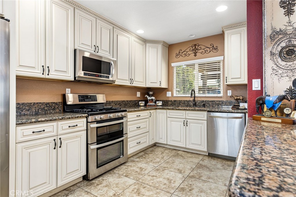 a white kitchen with stainless steel appliances granite countertop a stove a sink and a microwave
