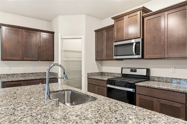a kitchen with granite countertop wooden cabinets a stove top oven and stainless steel appliances
