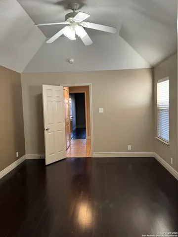 a view of an empty room with wooden floor and a ceiling fan