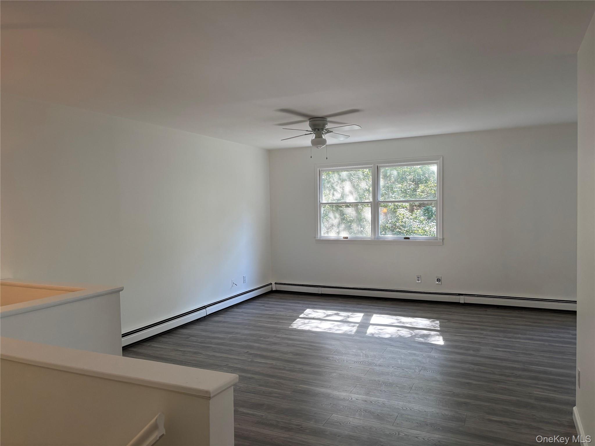 679 A Meadow Road Smithtown, NY 11787 - Photo 16 of 30 Empty room with dark wood-style flooring, baseboard heating, and ceiling fan