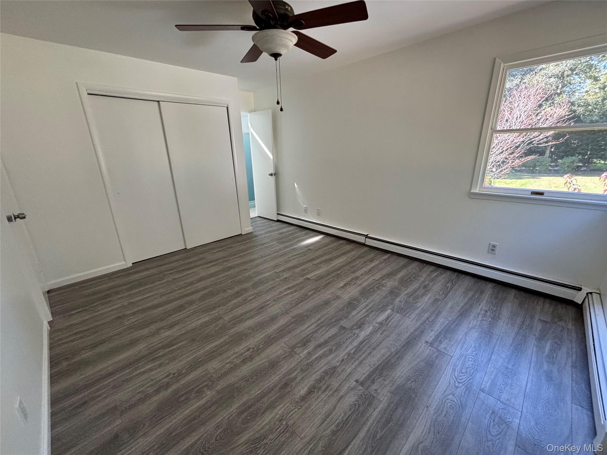 679 A Meadow Road Smithtown, NY 11787 - Photo 23 of 30 Unfurnished bedroom with dark wood-style flooring, a baseboard heating unit, a ceiling fan, and a closet