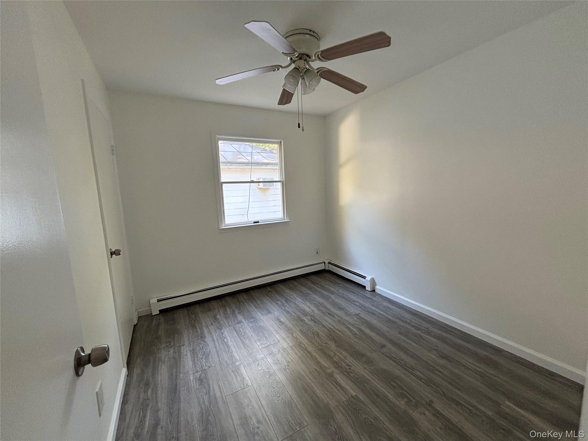 679 A Meadow Road Smithtown, NY 11787 - Photo 25 of 30 Unfurnished room featuring dark wood finished floors, ceiling fan, and a baseboard heating unit