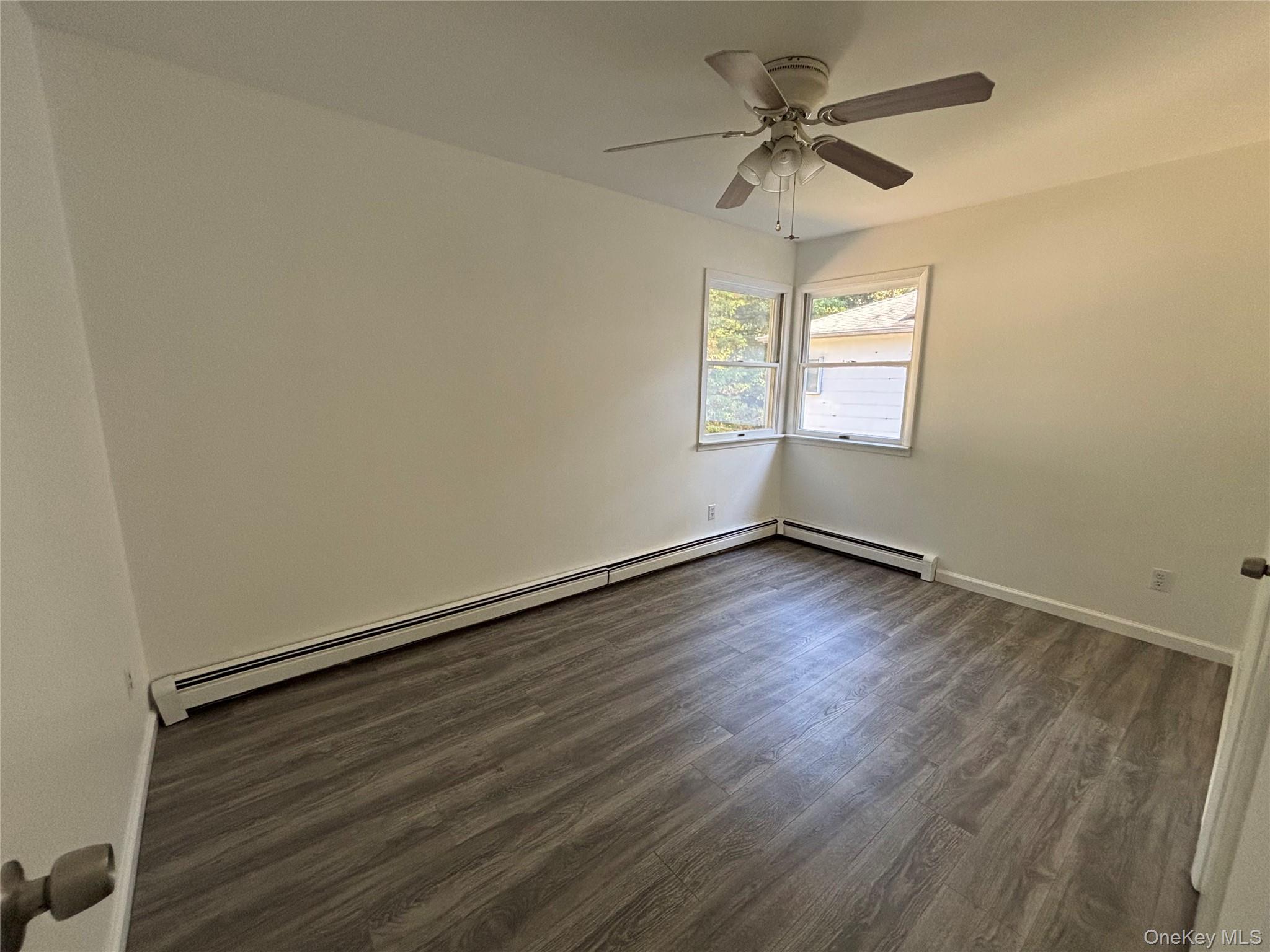 679 A Meadow Road Smithtown, NY 11787 - Photo 26 of 30 Spare room featuring dark wood-style floors, a baseboard heating unit, and ceiling fan