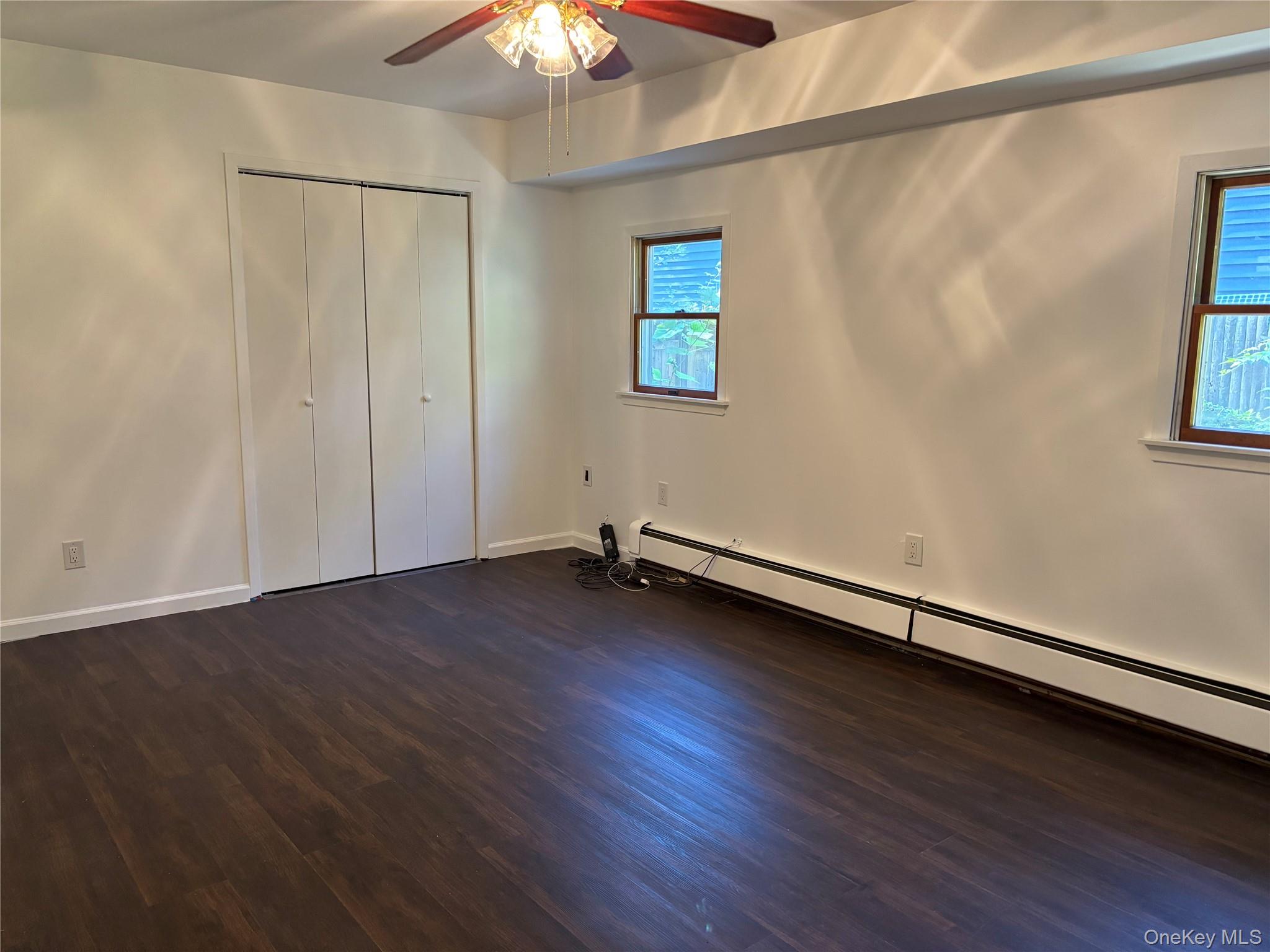 679 A Meadow Road Smithtown, NY 11787 - Photo 9 of 30 Unfurnished bedroom with a baseboard heating unit, dark wood finished floors, a ceiling fan, and a closet