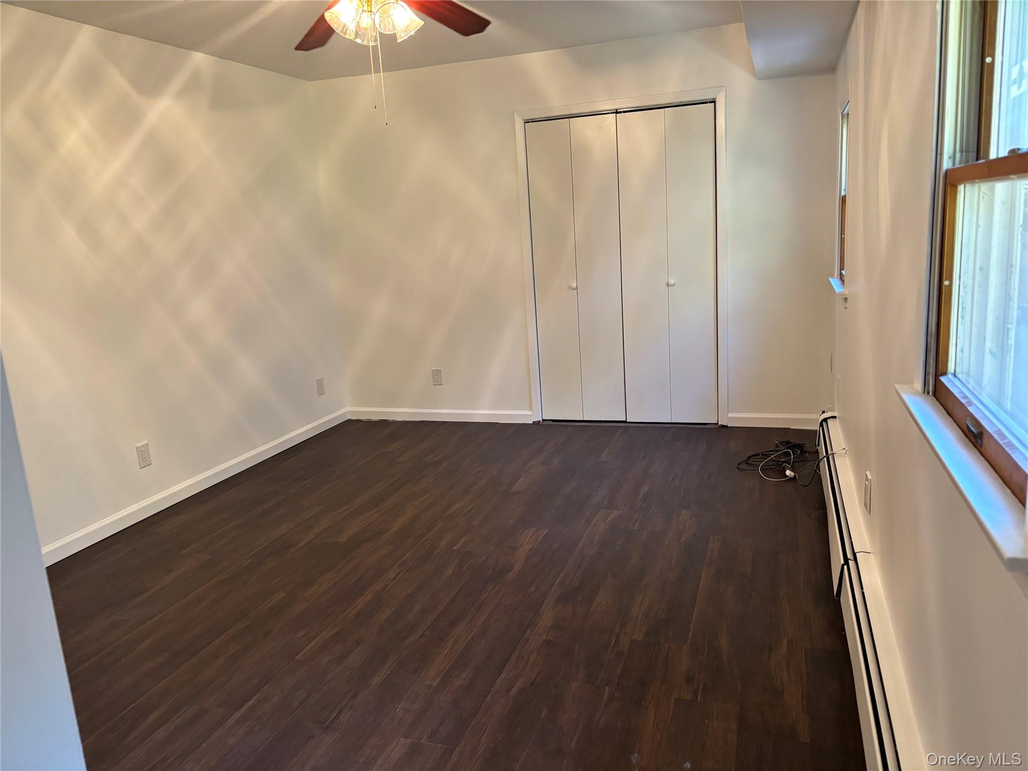 679 A Meadow Road Smithtown, NY 11787 - Photo 10 of 30 Unfurnished bedroom with baseboard heating, dark wood-style floors, ceiling fan, and a closet