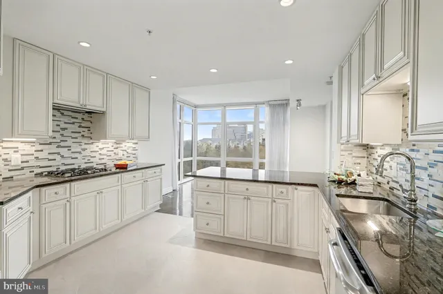 a large kitchen with granite countertop a sink and white cabinets