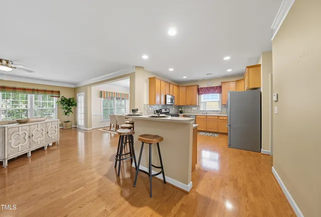 a kitchen with stainless steel appliances granite countertop a refrigerator a sink dishwasher and a dining table with wooden floor