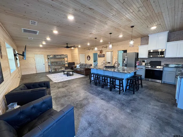 a living room with stainless steel appliances furniture a rug and a kitchen view