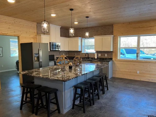 a kitchen with stainless steel appliances granite countertop a dining table chairs refrigerator sink and cabinets