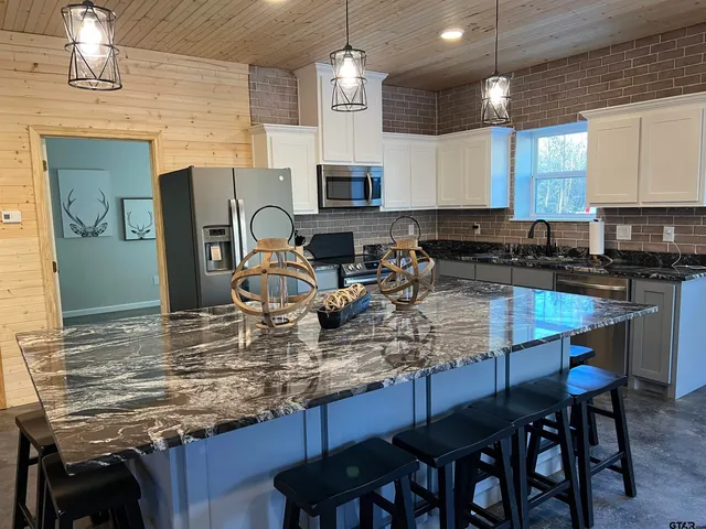 a kitchen with kitchen island granite countertop a table chairs stove a sink dishwasher and cabinets