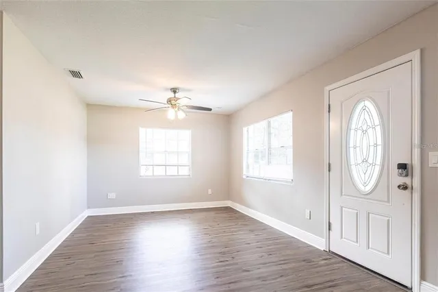 an empty room with wooden floor fan and windows