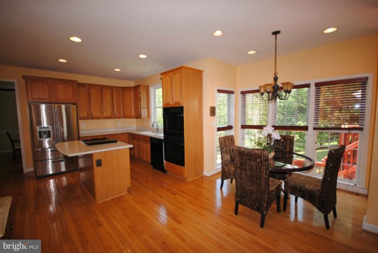 20334 Cliftons Point Street Sterling, VA 20165 - Photo 17 of 30 a kitchen with stainless steel appliances granite countertop a refrigerator a stove top oven a sink dishwasher a dining table and chairs with wooden floor