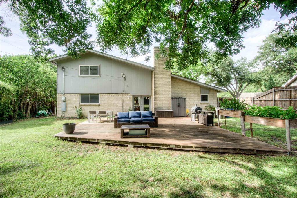12231 Veronica Road Farmers Branch, TX 75234 - Photo 24 of 26 Expansive backyard featuring a large wooden deck, mature trees providing natural shade, a brick-faced exterior, raised garden beds, and a fenced perimeter