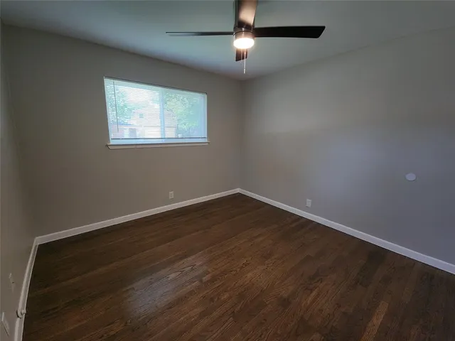 a view of an empty room with wooden floor and a ceiling fan