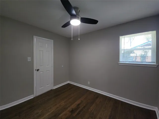 an empty room with wooden floor fan and windows