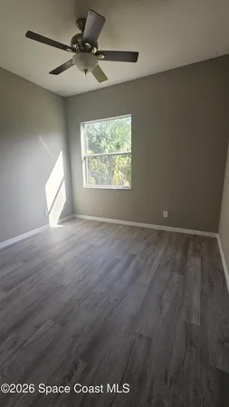 an empty room with wooden floor fan and windows