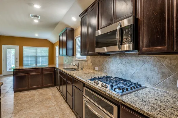 a kitchen with stainless steel appliances granite countertop wooden cabinets a stove top oven and granite counter tops