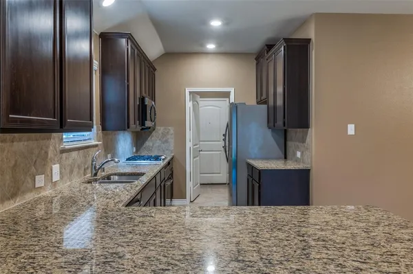 a kitchen with stainless steel appliances granite countertop a refrigerator a stove and a sink with wooden cabinets