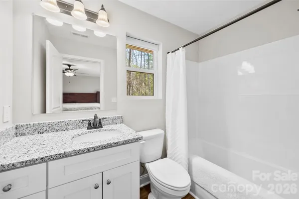 a bathroom with a granite countertop sink a toilet a mirror a vanity a bathtub and shower