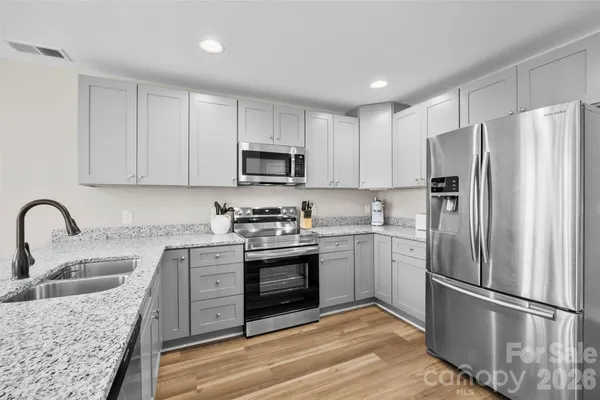 a kitchen with stainless steel appliances granite countertop a refrigerator stove a sink and white cabinets