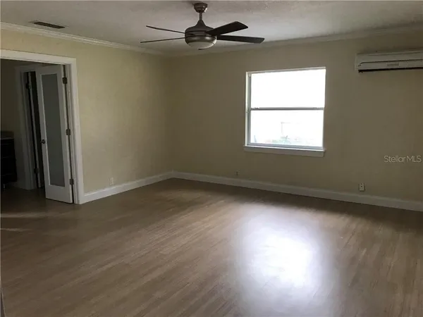 an empty room with wooden floor fan and windows