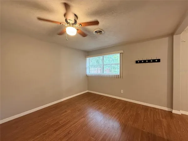 an empty room with wooden floor fan and windows