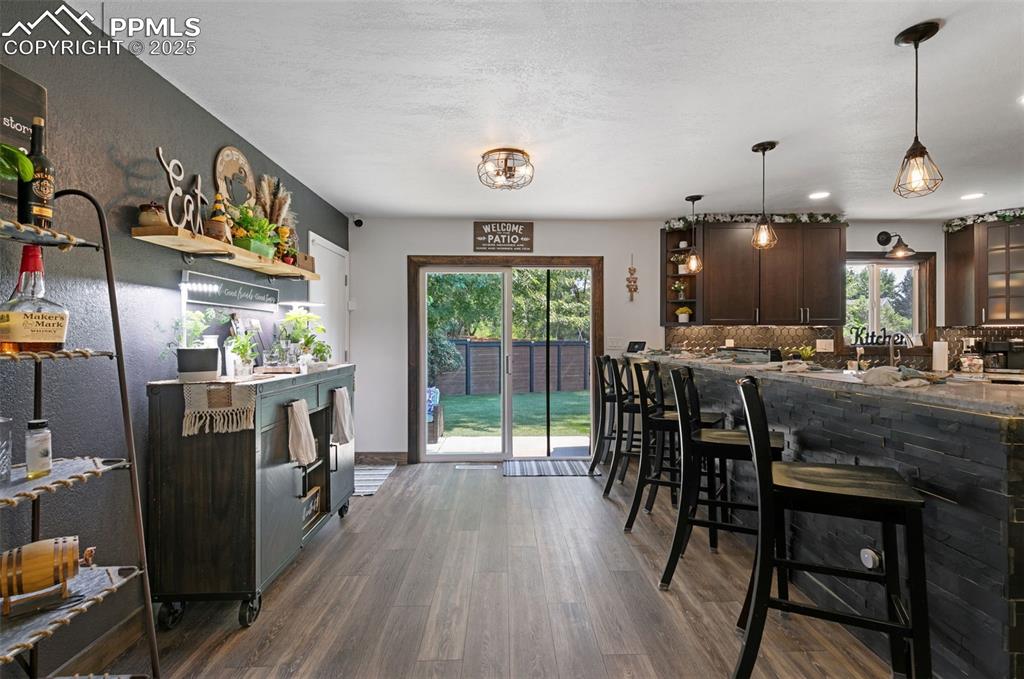 1921 Van Diest Road Colorado Springs, CO 80915 - Photo 11 of 45 Kitchen featuring dark brown cabinets, dark wood finished floors, hanging light fixtures, a breakfast bar, and tasteful backsplash