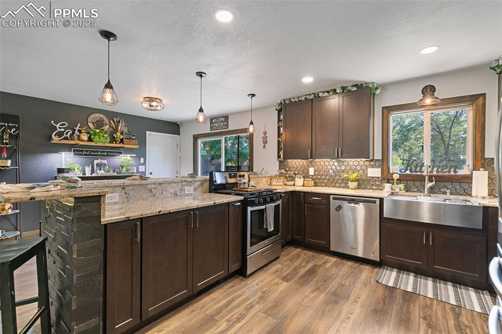 1921 Van Diest Road Colorado Springs, CO 80915 - Photo 33 of 45 Kitchen featuring dark brown cabinets, a peninsula, appliances with stainless steel finishes, light stone countertops, and dark wood-type flooring