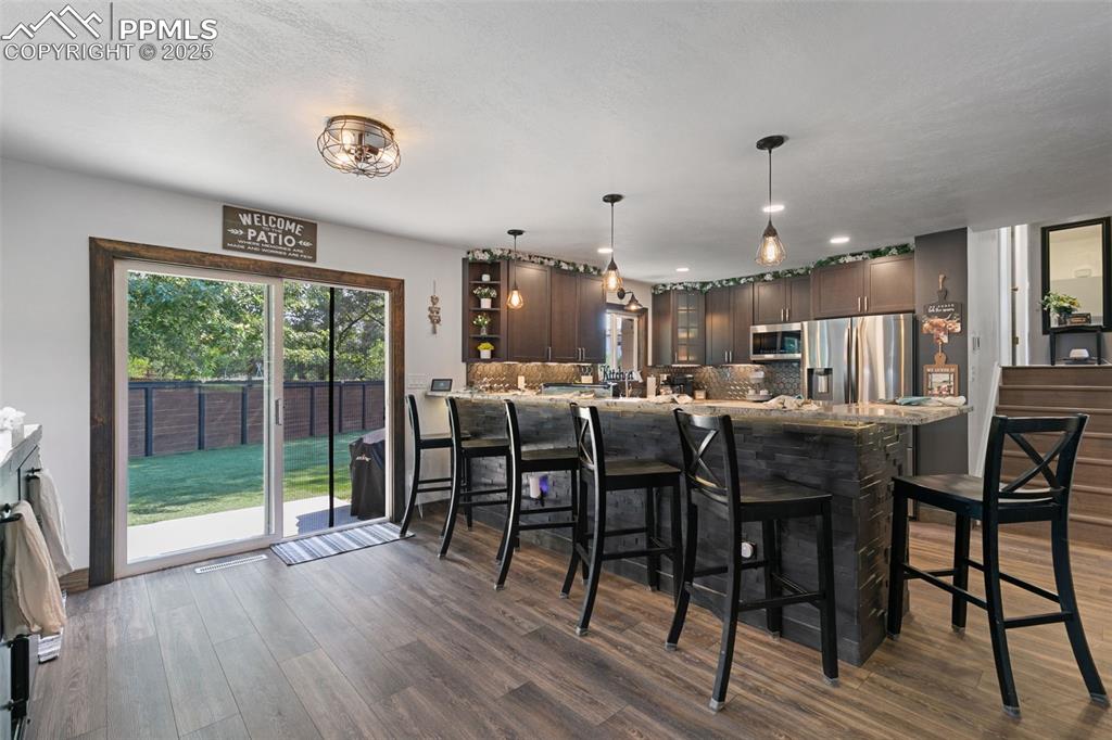 1921 Van Diest Road Colorado Springs, CO 80915 - Photo 10 of 45 Kitchen featuring dark brown cabinets, decorative backsplash, stainless steel appliances, a breakfast bar area, and dark wood-type flooring