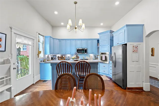 a kitchen with stainless steel appliances granite countertop a refrigerator a sink a stove a dining table and chairs with wooden floor