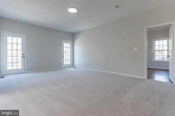 an empty room with windows and view of kitchen