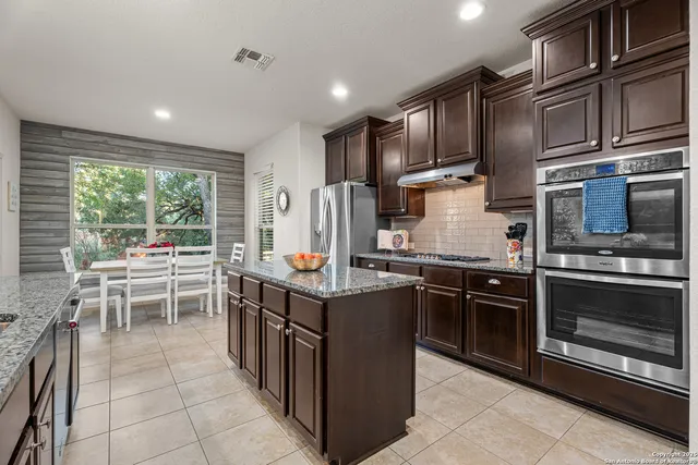 a kitchen with stainless steel appliances granite countertop a stove top oven a sink dishwasher a dining table and chairs with wooden cabinets
