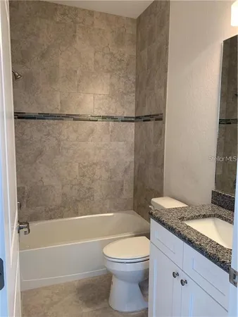 a bathroom with a granite countertop bathtub shower sink vanity and toilet