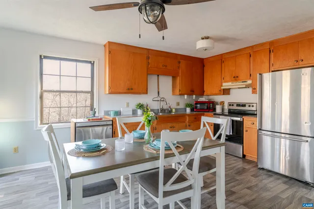 a kitchen with stainless steel appliances granite countertop a stove a refrigerator a microwave a dining table and chairs with wooden floor