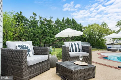 a view of a patio with couches table and chairs under an umbrella with large trees