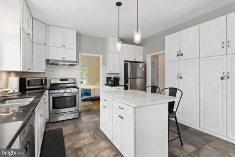 a kitchen with stainless steel appliances granite countertop a sink stove a refrigerator and white cabinets with wooden floor