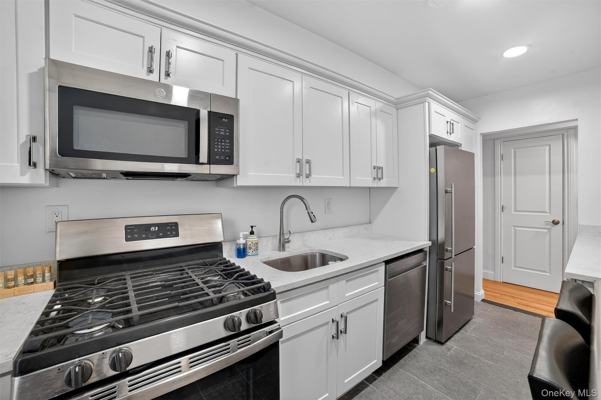 60 Locust Avenue, Unit 214A New Rochelle, NY 10801 - Photo 15 of 20 Kitchen with appliances with stainless steel finishes, white cabinetry, light stone counters, and dark tile patterned flooring