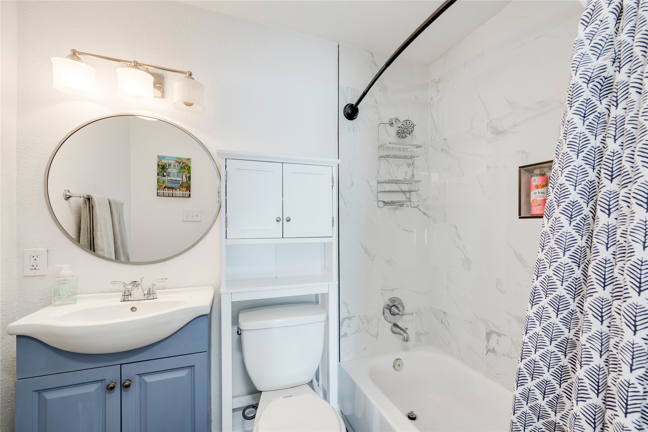 5300 Halmark Drive Austin, TX 78723 - Photo 24 of 40 A well-appointed bathroom features a crisp white shower with marble-look tiles and a charming blue vanity.