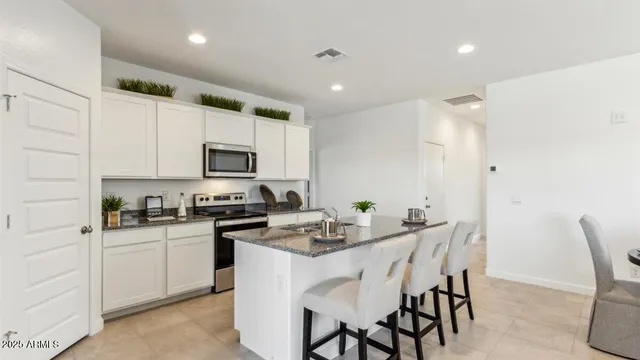 a kitchen with white cabinets a sink stove and chairs with wooden floor