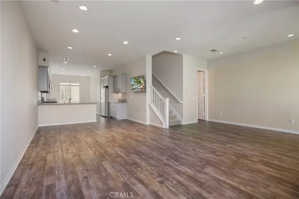 a view of empty room with wooden floor and kitchen