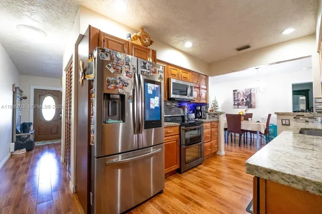 a kitchen with stainless steel appliances granite countertop a refrigerator a stove top oven a sink dishwasher and dining table with wooden floor