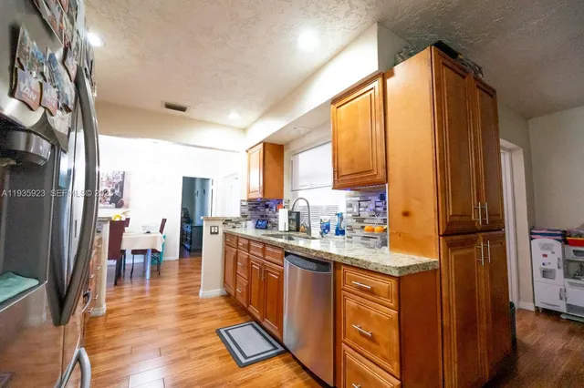 a kitchen with stainless steel appliances granite countertop a refrigerator a sink dishwasher a stove and a dining table with wooden floor