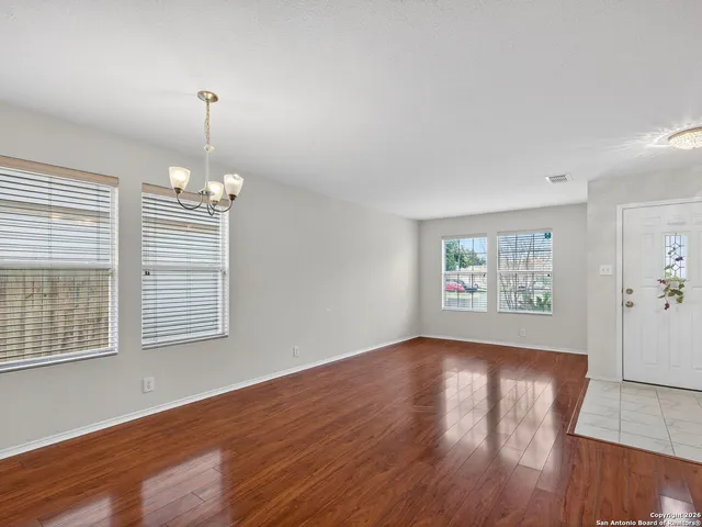 an empty room with wooden floor chandelier and windows