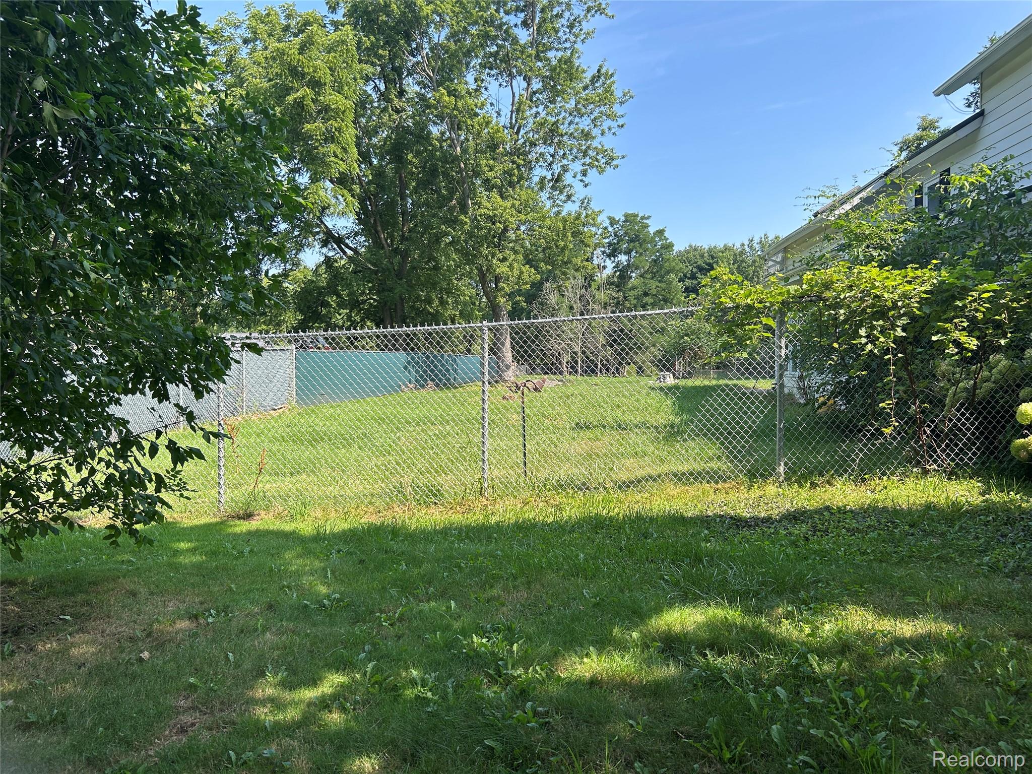 1285 Grange Hall Road Fenton, MI 48430 - Photo 41 of 50 Expansive backyard featuring a chain-link fence, mature trees, and a grassy area