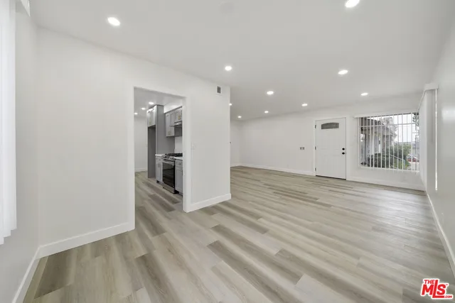 an empty room with wooden floor and a kitchen