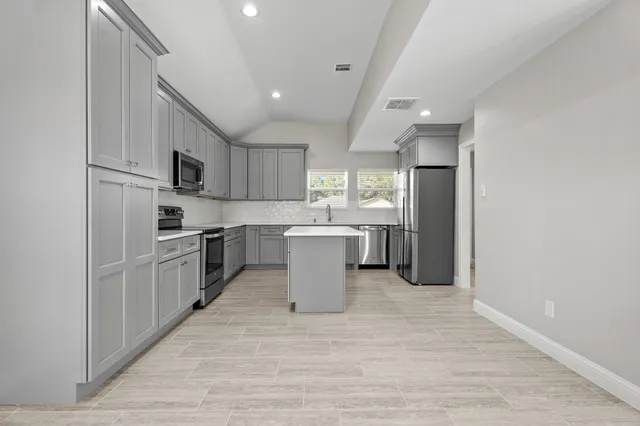 a large kitchen with a large counter top a sink stainless steel appliances and cabinets