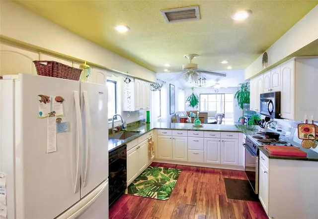 a kitchen with stainless steel appliances a refrigerator a sink dishwasher a stove and white cabinets with wooden floor
