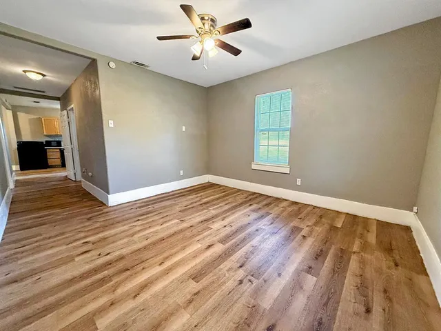 an empty room with wooden floor chandelier fan and windows