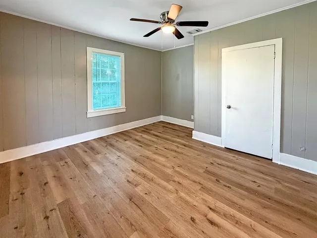 an empty room with wooden floor ceiling fan and windows